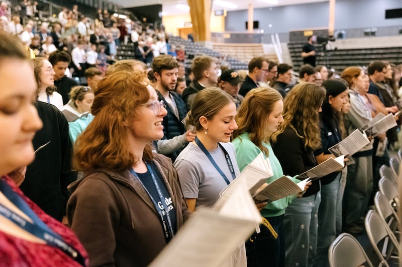 Adultos jóvenes se ponen de pie para cantar durante una devoción conmemorativa de "100 años del instituto" celebrada en el ICCU Arena en el campus de la Universidad de Idaho en Moscow, Idaho, el sábado 26 de septiembre de 2026.