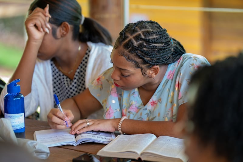 Una joven toma notas en una guía Para la fortaleza de la juventud con sus Escrituras a su lado sobre una mesa en la República Dominicana en julio de 2025.