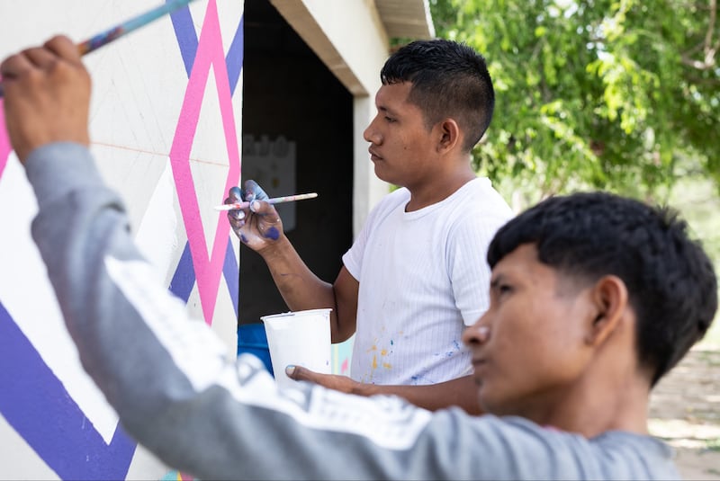 Keiber Epinayu, atrás, pinta símbolos antiguos Kanaas en infraestructura de agua con un joven Wayúu en La Guajira, Colombia en febrero de 2024.