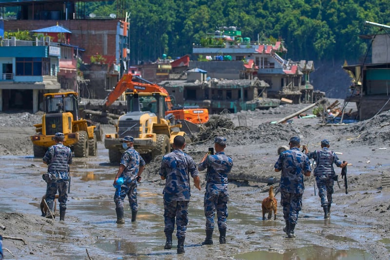 Policías nepalíes observan mientras las máquinas excavadoras limpian los escombros de las inundaciones repentinas en el distrito de Nuwakot de Nepal, jueves 27 de agosto de 2026.