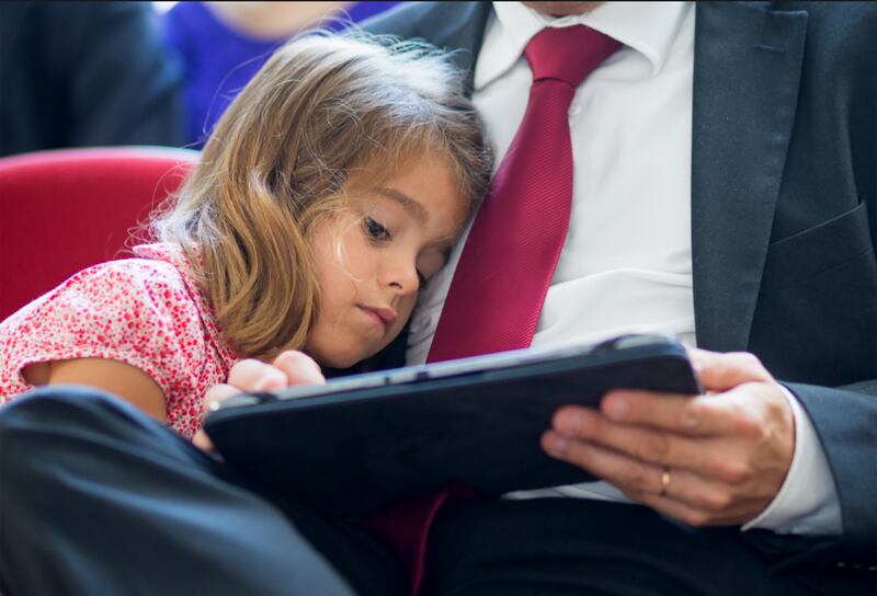 Una hija se apoya en su padre mientras lee en una tableta.