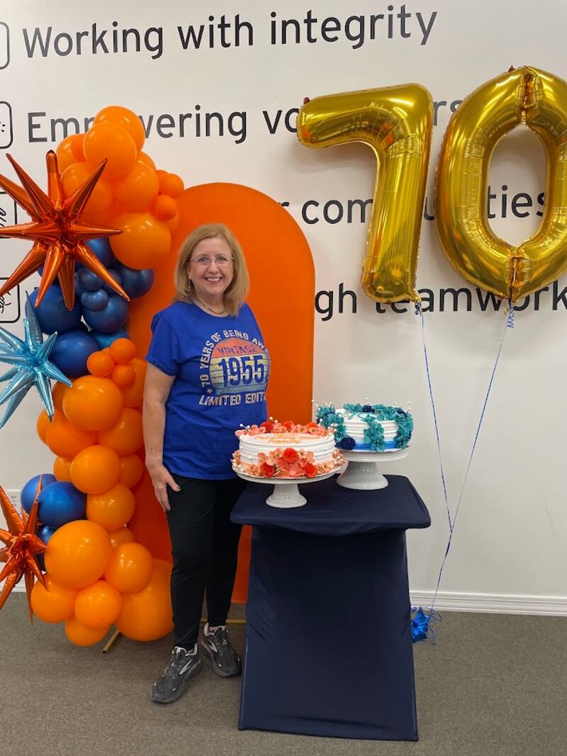 Gwynne Fullmer posa para una foto con pasteles de cumpleaños y globos mientras ofrece servicio como voluntaria en el Midwest Food Bank en Gilbert, Arizona, el 18 de octubre de 2025, para celebrar su cumpleaños número 70.