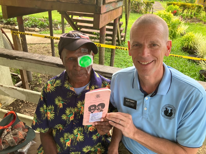 El pastor Ronny, a la izquierda, se toma una foto con el élder Bret Dandoy, a la derecha, mientras sostiene su libreta de registros médicos después de una cirugía de cataratas en 2026.