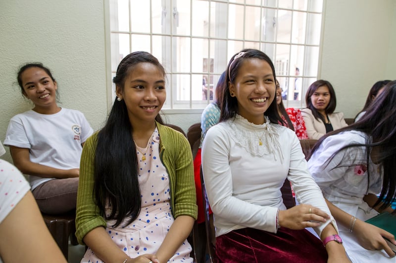Jóvenes mujeres en Filipinas se sientan juntas en clase y sonríen.