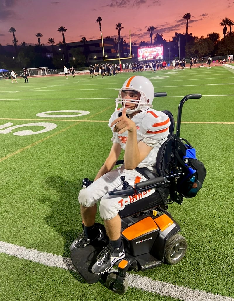 Matthew Cooper usa su uniforme de fútbol americano en su silla de ruedas durante un partido de fútbol de la escuela secundaria en el otoño de 2024.