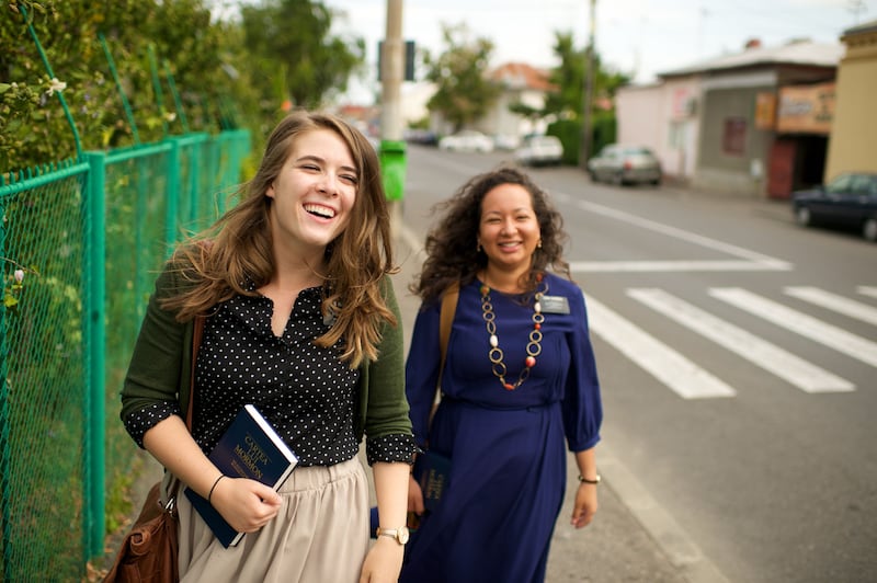 Dos misioneras en Rumania se ríen mientras caminan juntas por una calle.