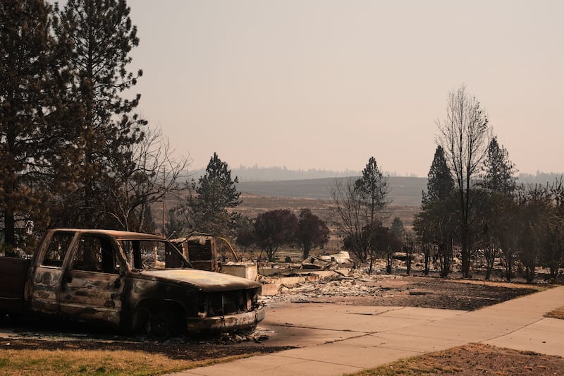 Un camión quemado se encuentra en una entrada de garaje cerca de varias casas destruidas en un vecindario residencial el martes, 4 de agosto de 2026, después de que un incendio forestal azotara la parte norte de Spokane, Washington.
