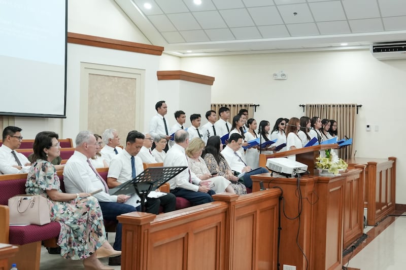 El élder Ulisses Soares, del Cuórum de los Doce Apóstoles, y su esposa, la hermana Rosana Soares, a la izquierda, escuchan mientras un coro canta durante un devocional de jóvenes adultos en Cebú el 16 de mayo de 2026.