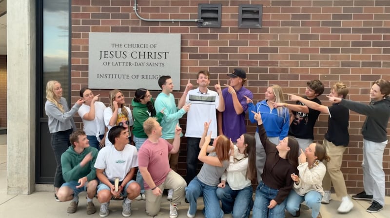 Kaleb Jones, en el centro, señala hacia el cielo mientras otros adultos jóvenes lo señalan a él en un video filmado en el Instituto de Religión del Valle de Utah en Orem, Utah, en 2026.