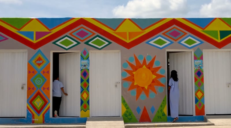 Dos jóvenes de la comunidad Wayúu entran a un nuevo edificio con inodoros, grifos y lavamanos después de que fueron pintados al estilo Kanaas en La Guajira, Colombia, en febrero de 2024.