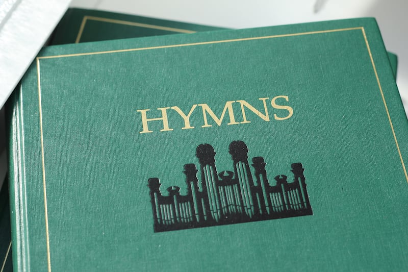 El himnario verde de la Iglesia, enfocado en el título "Hymns" y el símbolo del Tabernáculo.