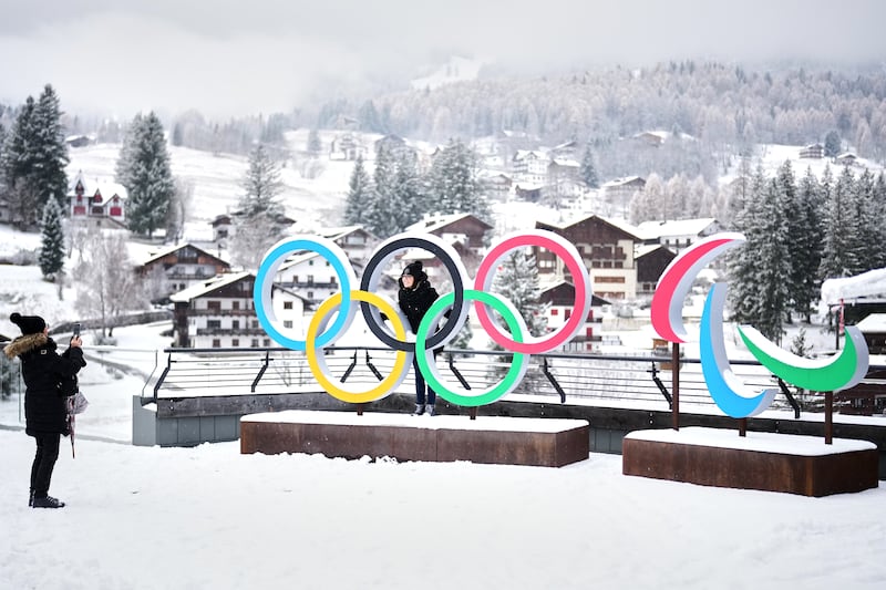 Personas toman fotos frente a los aros de los Juegos Olímpicos de Invierno y las medias lunas de los Juegos Paralímpicos de Milán Cortina, en Cortina D'Ampezzo, el 20 de noviembre de 2025.