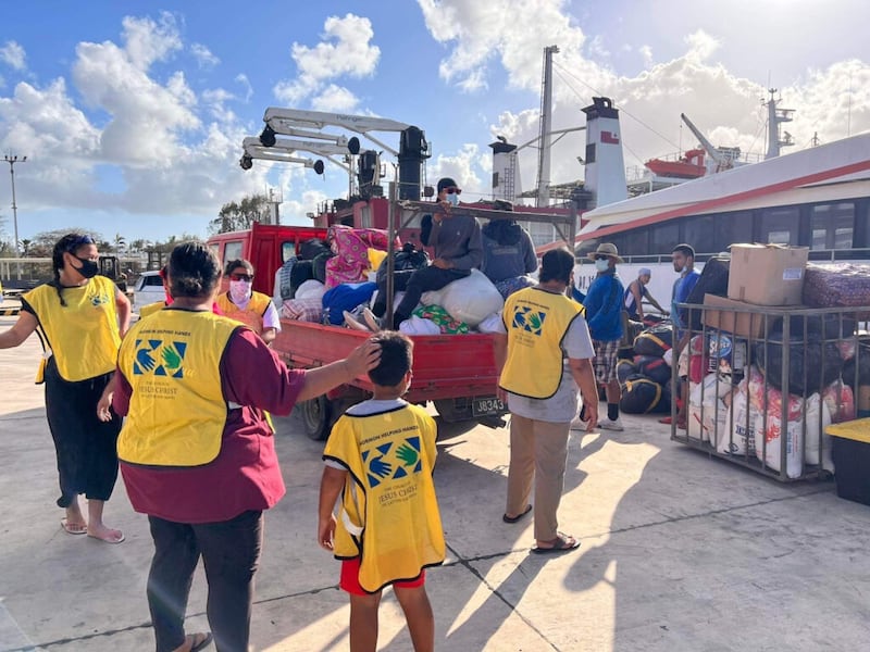 Después de que una erupción volcánica en alta mar desencadenó un tsunami en Tonga, el sábado 15 de enero de 2022,los voluntarios de las estacas en Tongatapu, Tonga, ayudan a descargar suministros donados listos para cargar en un buque con destino a las islas exteriores.