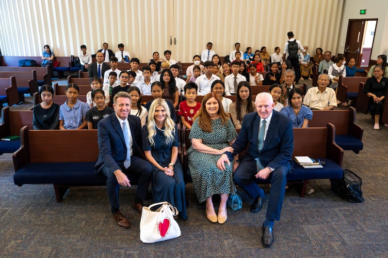El presidente general de los Hombres Jóvenes, Timothy L. Farnes, a la izquierda, su esposa, la hermana Linsey Farnes, la hermana Terri Johnson y su esposo, el élder Kelly R. Johnson, una Autoridad General Setenta y presidente del Área Asia, se toman una foto con jóvenes en Camboya después de un devocional en mayo de 2026.