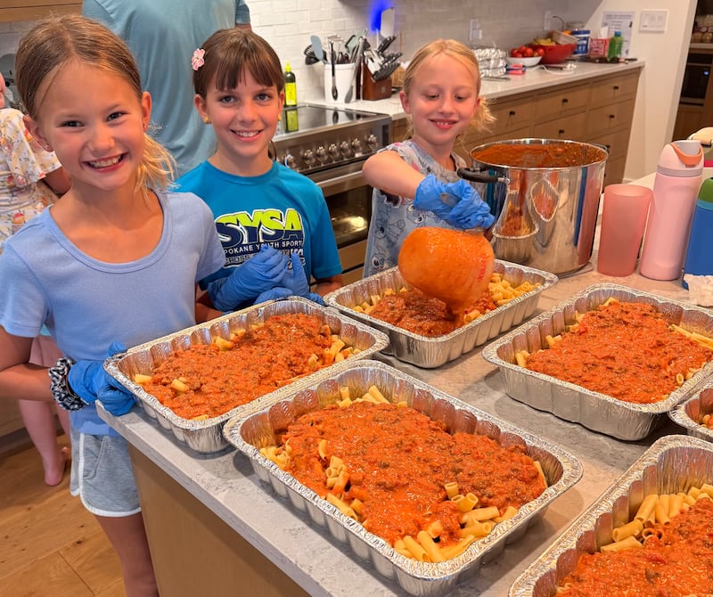 De izquierda a derecha, Sadie Coons, Adeline King y Hannah Shafer ayudan a su grupo de Días de Actividades para Niñas de la rama a preparar comidas para llevar a las familias desplazadas por incendios forestales en Spokane, Washington, en agosto de 2026.