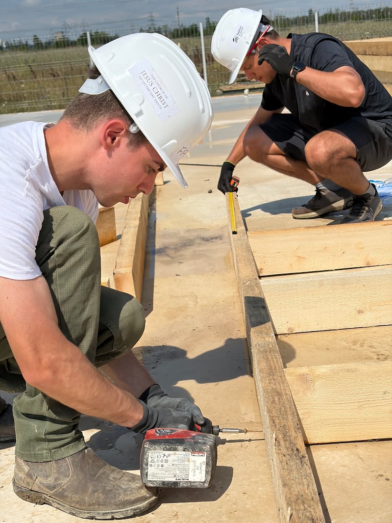 Adultos jóvenes miden y ensamblan marcos de paredes de madera para casas en construcción en un proyecto de servicio de Hábitat para la Humanidad Rumania en Berceni, Rumania, en agosto de 2026.