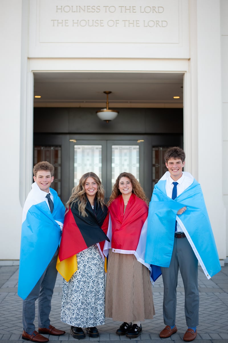 Isaac, Elle, Isabel y Eli Reid posan para una foto con banderas que representan los lugares donde servirán en sus misiones, colocadas sobre sus hombros.