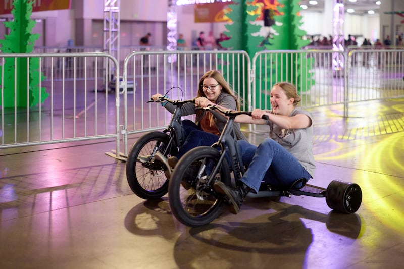Dos mujeres participan en una carrera de triciclos en el Centro de Convenciones Salt Palace durante la Conferencia de Jóvenes Adultos del Área de Utah de 2026 en Salt Lake City el viernes, 14 de agosto de 2026.
