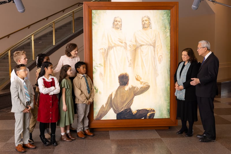El élder Gerrit W. Gong, la hermana Susan Gong y la presidenta Susan H. Porter conversan con seis niños junto a un retrato de la Primera Visión en el Centro de Conferencias de Salt Lake City durante la grabación de Amigo a Amigo, que se publicó el domingo, 24 de mayo de 2026.