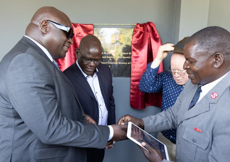 Fredrick Haga — director nacional keniano de educación para personas con necesidades especiales, a la izquierda — recibe la llave para inaugurar oficialmente el primer aula del nuevo centro de aprendizaje de la Escuela de Educación Especial Secundaria de Kibos de parte del mayor Omuse, capellán de la Escuela de Educación Especial Secundaria de Kibos. Cosmas Onywera — coordinador de educación para personas con necesidades especiales del condado de Kisumu, segundo desde la izquierda — y el director de la escuela, Joshua Ombayo, segundo desde la derecha, observan la presentación en Kisumu, Kenia, el 16 de enero de 2026.