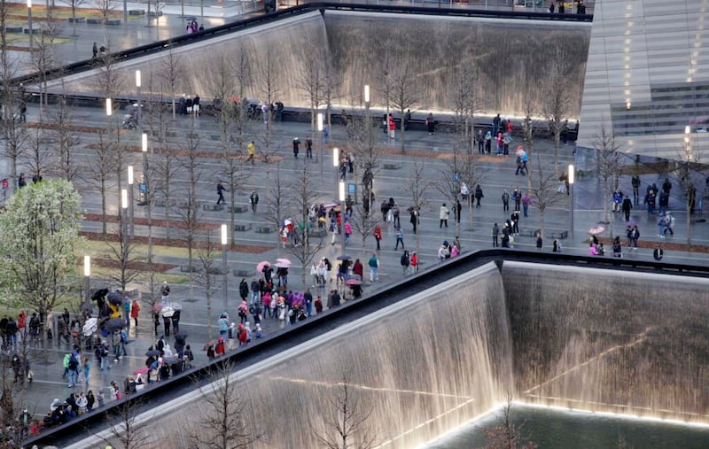 Los visitantes del Monumento Nacional 11 de septiembre caminan alrededor de las dos piscinas reflectantes, el domingo, 1 de abril de 2012 en Nueva York. Los nombres de las víctimas de los ataques terroristas del 11 de septiembre de 2001 están grabados en paneles de bronce alrededor de las piscinas. El Árbol Sobreviviente, a la izquierda, es un peral que sufrió graves daños en los ataques, fue rescatado y replantado en el monumento. (Foto AP / Mark Lennihan).