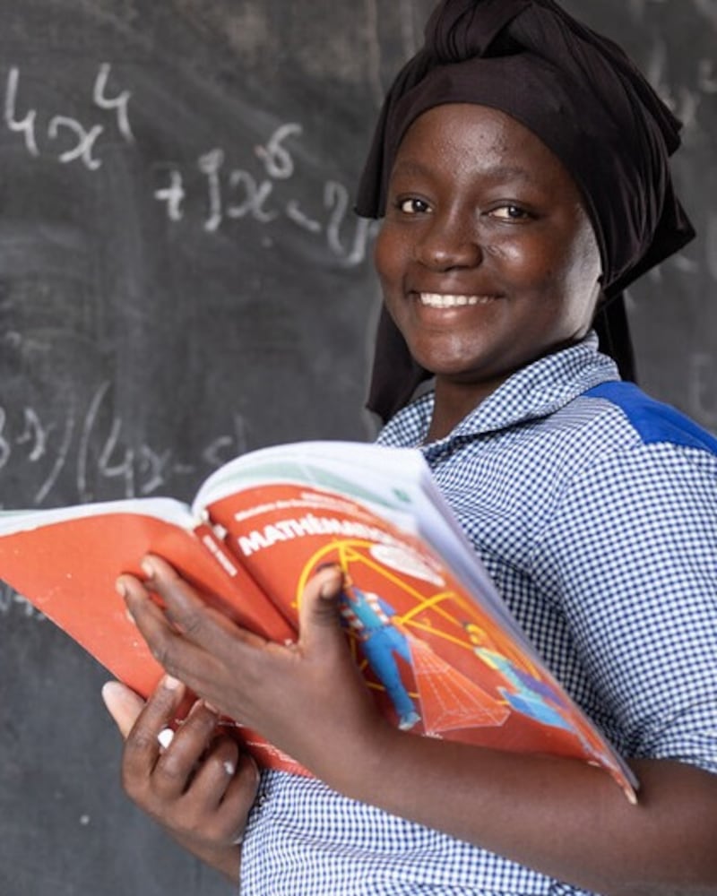Bibata Fofana posa para una foto con un libro de texto de matemáticas en Burkina Faso en 2024 después de la donación de un pozo por parte de la Iglesia. Fofana espera convertirse en maestra.