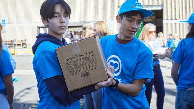 Dos jóvenes trasladan cajas de una donación de alimentos de America 250 en el área de Irvine, California, el sábado 21 de febrero de 2026.