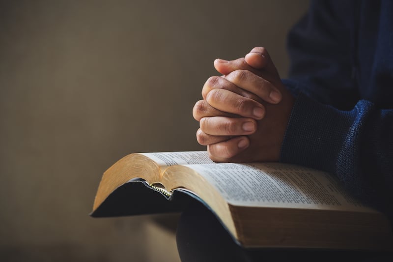 Las manos están cruzadas en oración sobre una Santa Biblia.
