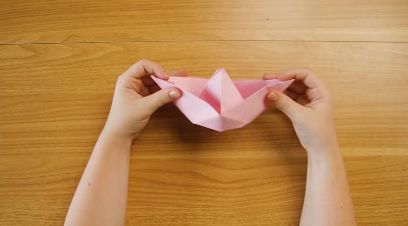 Un niño dobla un papel en forma de barco, como el arca de Noé.