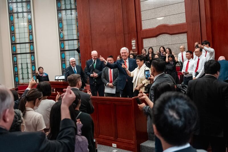El élder Dieter F. Uchtdorf y la hermana Harriet Uchtdorf se despiden con una señal de mano en forma de mini corazón de los miembros de Hong Kong.