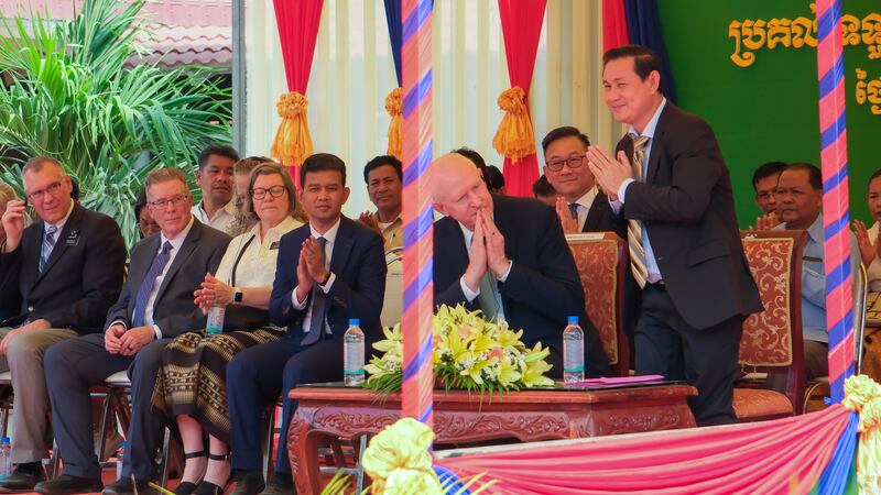El élder Kelly R. Johnson y el vicegobernador Nhek Ban Kheng ofrecen saludos tradicionales de sampeah, con ambas palmas juntas y los dedos extendidos con una inclinación de la cabeza, a las multitudes reunidas en la ceremonia de entrega que celebra la renovación de los hospitales en la provincia de Kampong Thom.