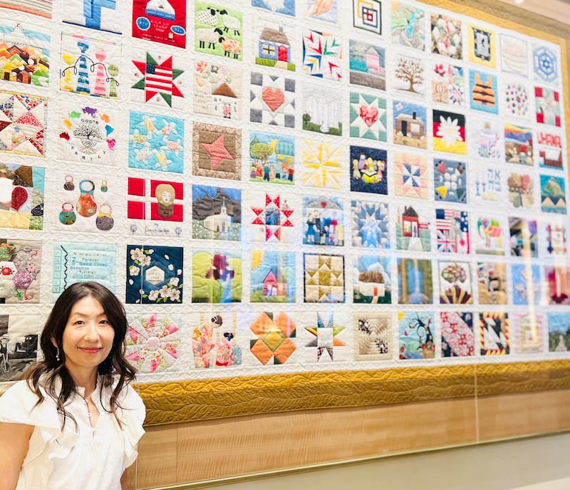 Sachiko Aldous se encuentra junto a la exhibición "The Family Quilt" en el Centro de Visitantes de Temple Square en Salt Lake City, julio de 2026.