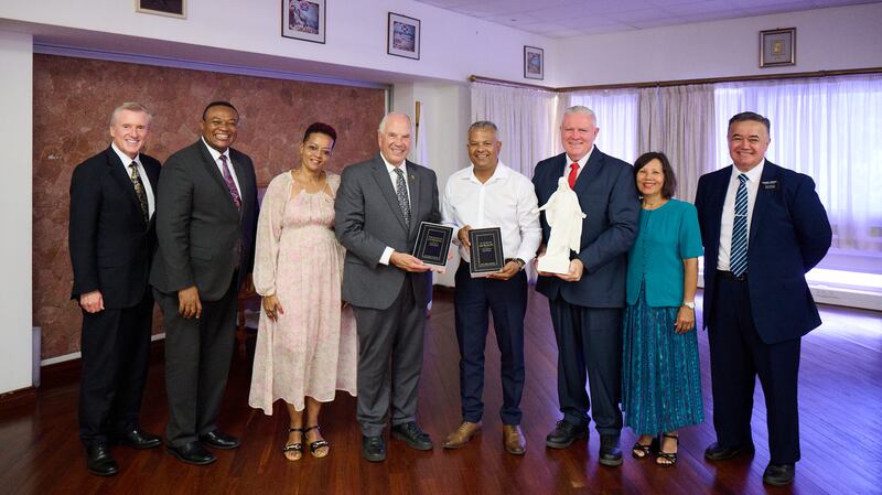 El élder Ronald A. Rasband junto a Sebastien Pillay, el vicepresidente de Seychelles, mientras sostienen dos ejemplares del Libro de Mormón, en Victoria, Seychelles, el 29 de octubre de 2025. También aparecen el élder Kevin R. Duncan, el élder Thierry K. Mutombo, Deborah Maimee, el élder Evan Healy y la hermana Marie Healy, y el presidente de la Misión Kenia Nairobi Este, David T. Onekawa.