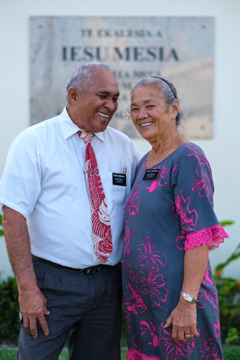 Una pareja de misioneros de edad avanzada está de pie cerca de una capilla de La Iglesia de Jesucristo de los Santos de los Últimos Días en Tahití en 2026.