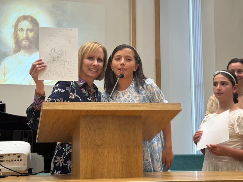 La hermana Amy A. Wright, primera consejera de la presidencia general de la Primaria, está de pie en el púlpito con una niña de la Primaria durante una asamblea devocional para niños de la Primaria en Breda, Países Bajos, el 6 de septiembre de 2025.