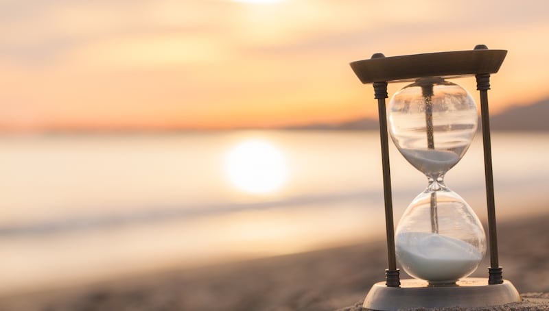 Un reloj de arena está en la playa mientras sale el sol.