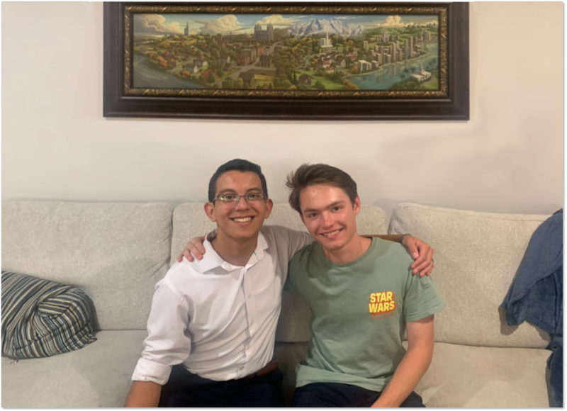 Oscar Hernández y Benjamín Woodworth se toman una foto juntos en la casa de los Woodworth en Utah, con la portada de "Santos" en la pared detrás de ellos en 2024.