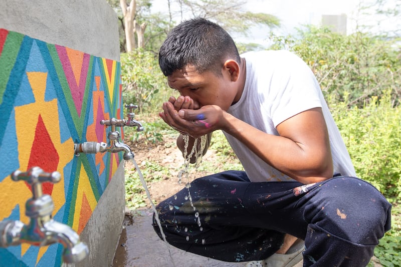Keiber Epinayu, un joven artista y líder de la comunidad wayúu, bebe agua de un nuevo grifo después de pintar la infraestructura en La Guajira, Colombia, en febrero de 2024.