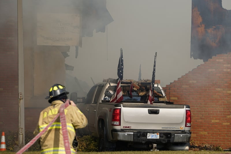 Un vehículo que fue estrellado contra el edificio de la Rama Grand Blanc está rodeado de humo mientras un bombero trabaja en la escena en Grand Blanc, Míchigan, domingo, 28 de septiembre de 2025.
