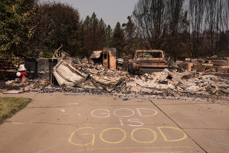 Un letrero que dice "Dios es bueno" está escrito en tiza junto a una boca de incendios y una casa quemada después de que un incendio forestal azotara la parte noroeste de Spokane, Washington, el martes, 4 de agosto de 2026.