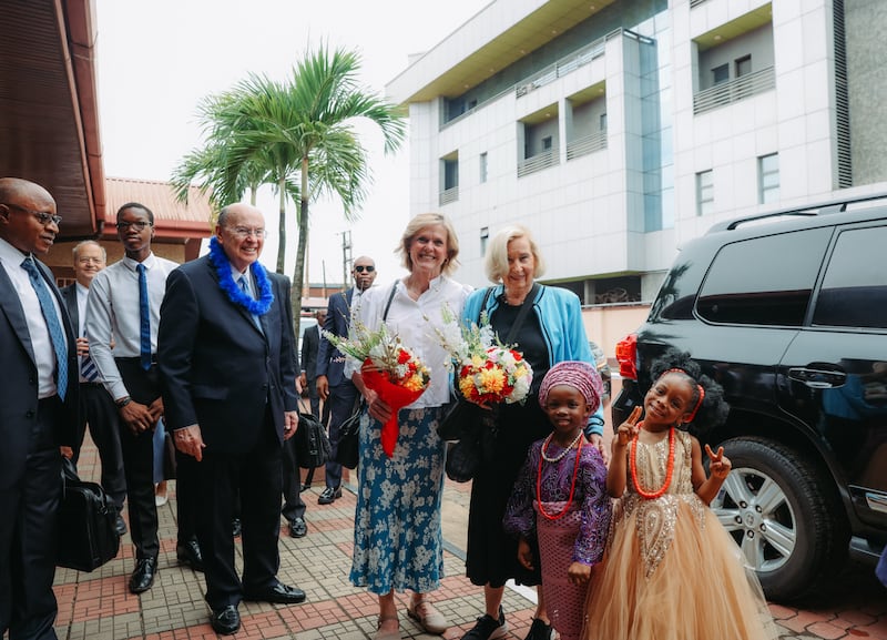 El élder Quentin L. Cook, la hermana Mary Cook, la hermana Rosalie Ringwood y otros son recibidos por dos pequeñas niñas nigerianas a su llegada al Centro de Estaca Lagos Nigeria Ikeja, el 14 de febrero de 2026.