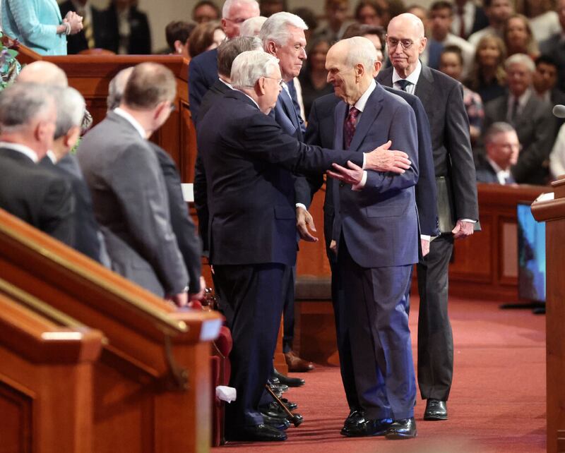 El presidente M. Russell Ballard, presidente en funciones del Cuórum de los Doce Apóstoles de la Iglesia de Jesucristo de los Santos de los Últimos Días, en el centro, saluda al presidente de la Iglesia Russell M. Nelson durante la Conferencia General Anual N° 192 en el Centro de Conferencias de Salt Lake City el sábado 2 de abril de 2022.