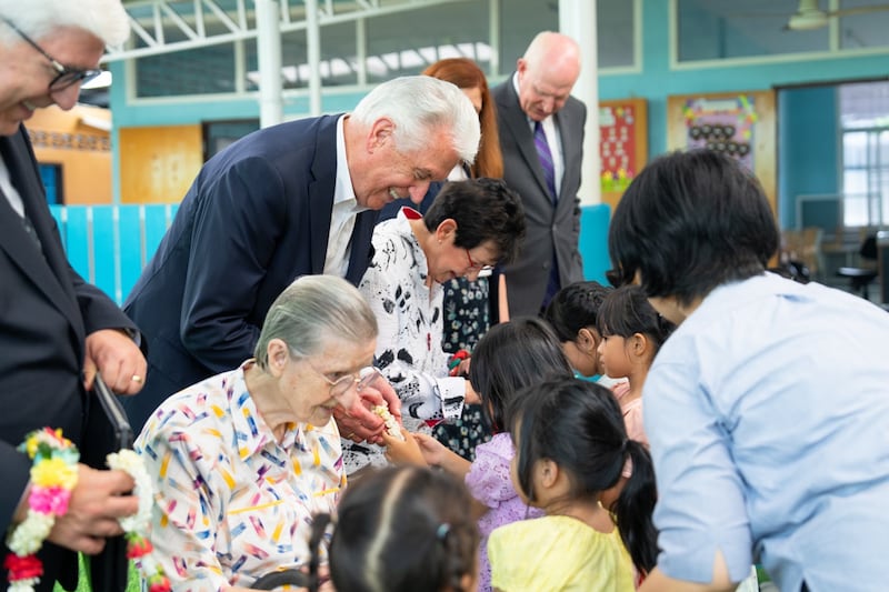 El Élder Dieter F. Uchtdorf y la hermana Harriet Uchtdorf saludan a los niños junto a la hermana Louise Horgan en Good Shepherd Sisters Bangkok.