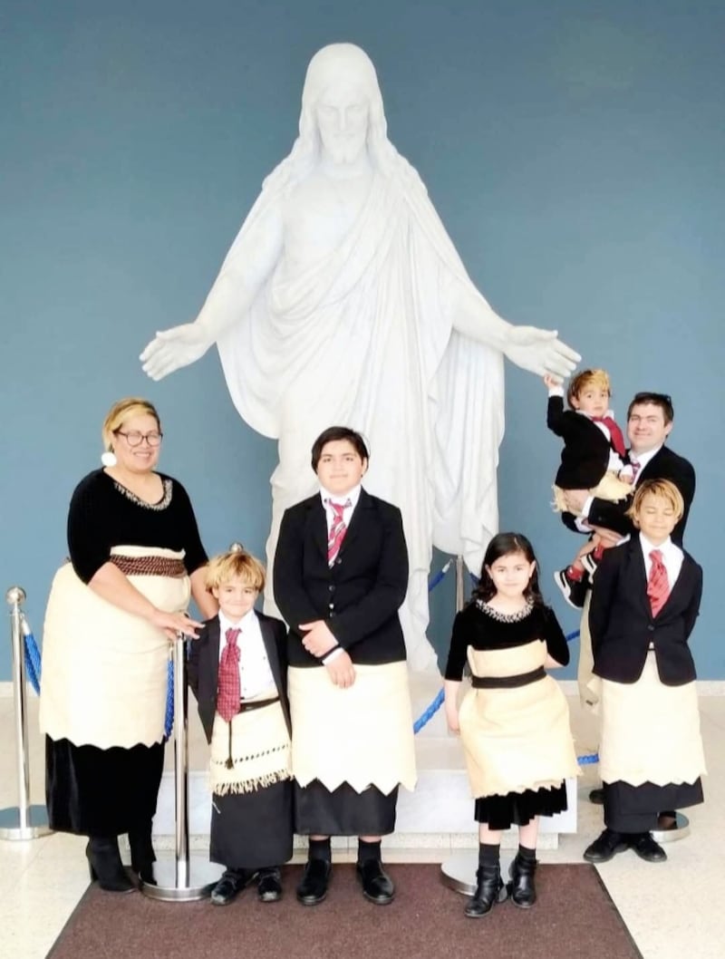 La familia Strom fotografiada frente a una estatua del Cristus con vestimenta tradicional tongana a principios de agosto de 2022 en el Templo de Hamilton, Nueva Zelanda.