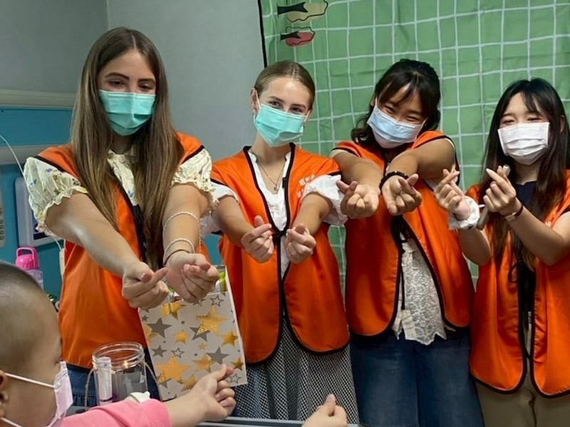 Adultos jóvenes de La Iglesia de Jesucristo de los Santos de los Últimos Días hacen gestos de corazón con una joven paciente con cáncer en un hospital infantil en la ciudad de Changhua, Taiwán. Los adultos jóvenes visitan el hospital dos veces al mes para compartir clases de musicoterapia y arteterapia.