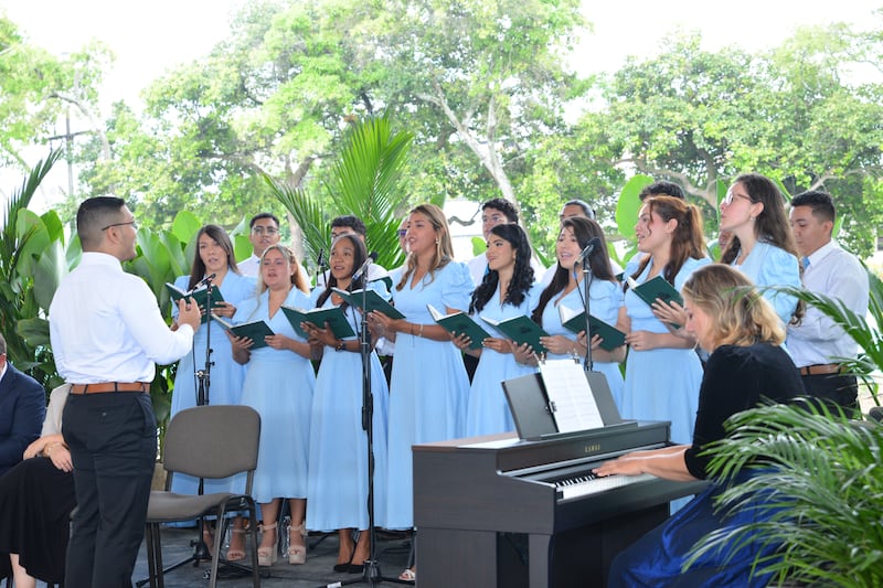 Un coro de mujeres con vestidos azul claro cantando al aire libre.