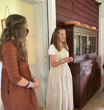 La hermana Olivia Graysen, a la izquierda, y la hermana Marissa Bischoff presentan un recorrido por el interior de la casa histórica de José y Emma Smith en el sitio de la Restauración del sacerdocio en Oakland Township (Susquehanna), Pensilvania, el domingo, 29 de agosto de 2021. A la derecha está el élder Neil L. Andersen y la hermana Kathy Andersen.