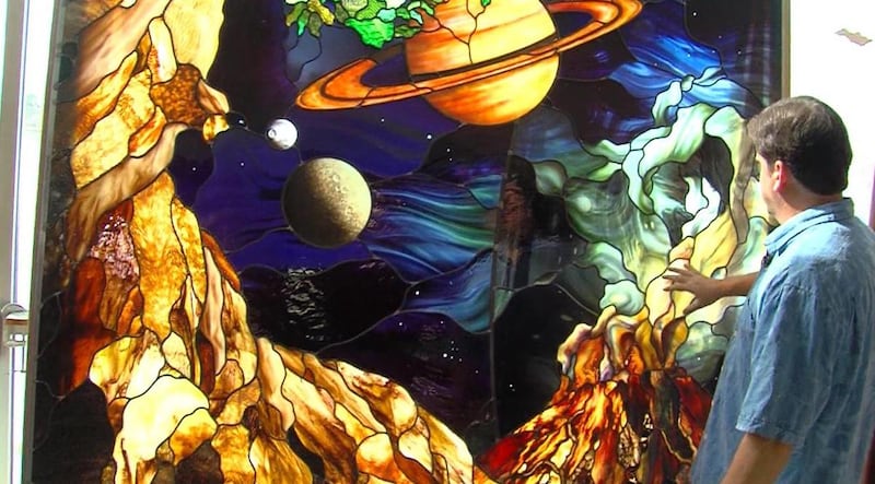 El artista de vidrio de color Tom Holdman muestra uno de los paneles de vidrio que su estudio creó para la celebración del 75 aniversario de la Universidad del Valle de Utah en 2017.