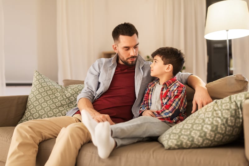 Un padre e hijo conversan mientras están sentados en un sofá.