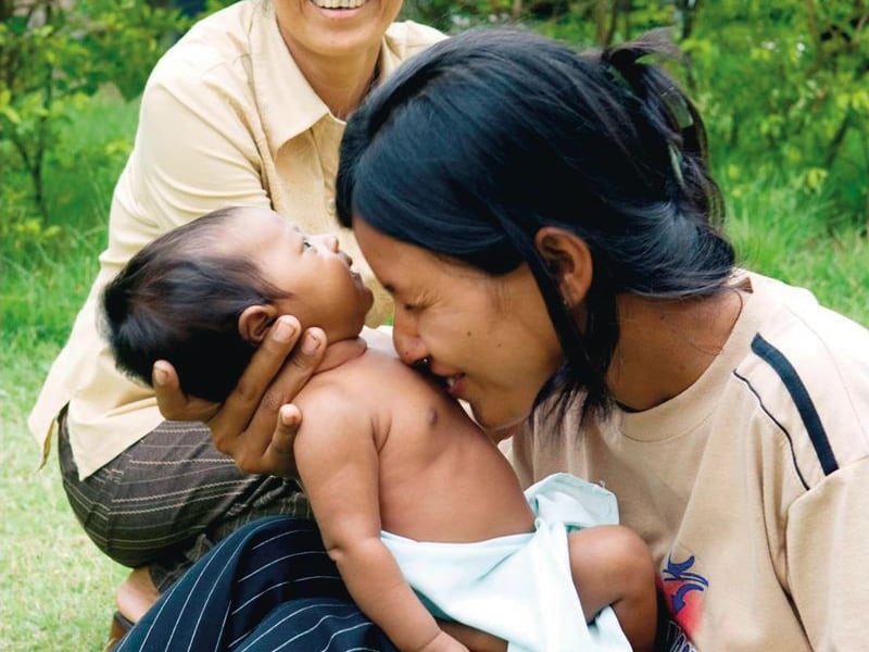 Una joven madre sostiene a su bebé en Camboya mientras otra mujer observa.